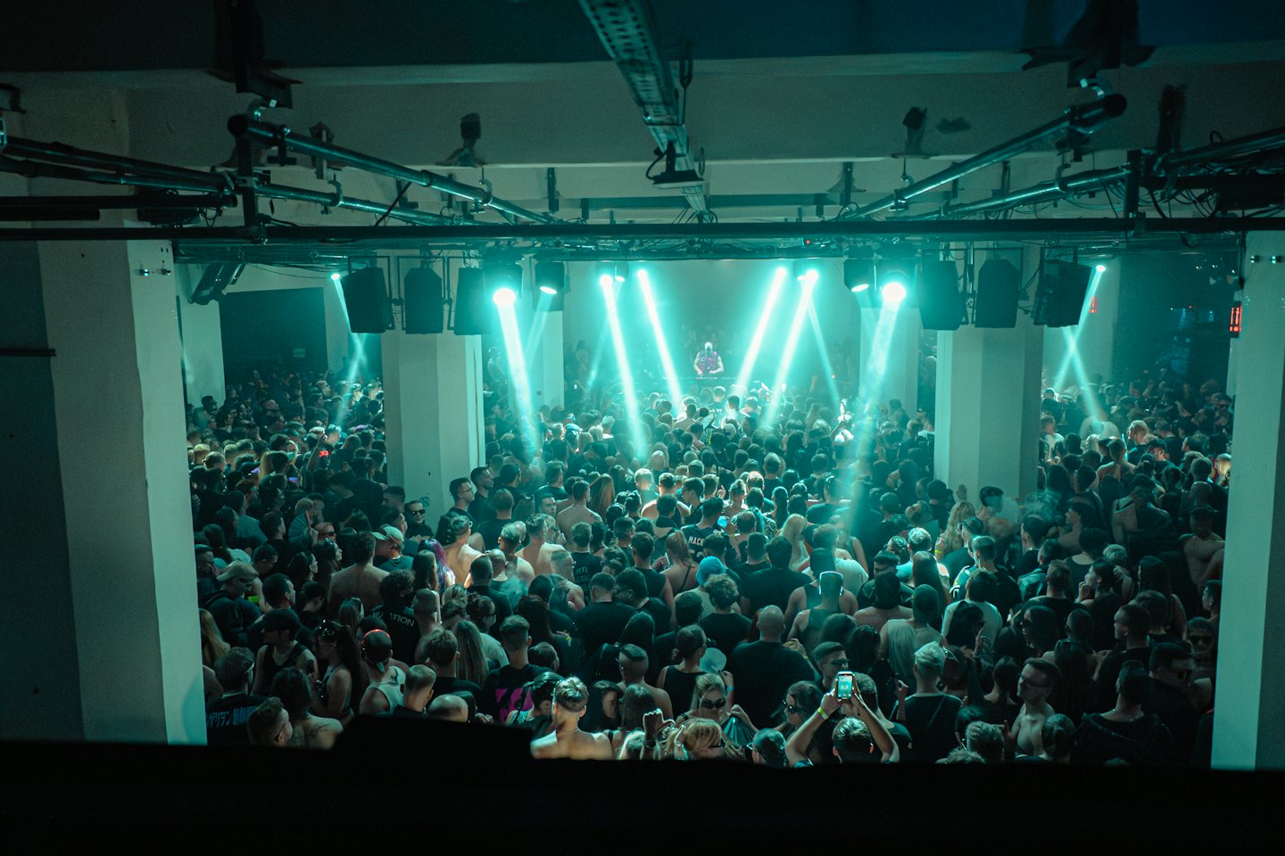 A large crowd dances together at an indoor music concert.