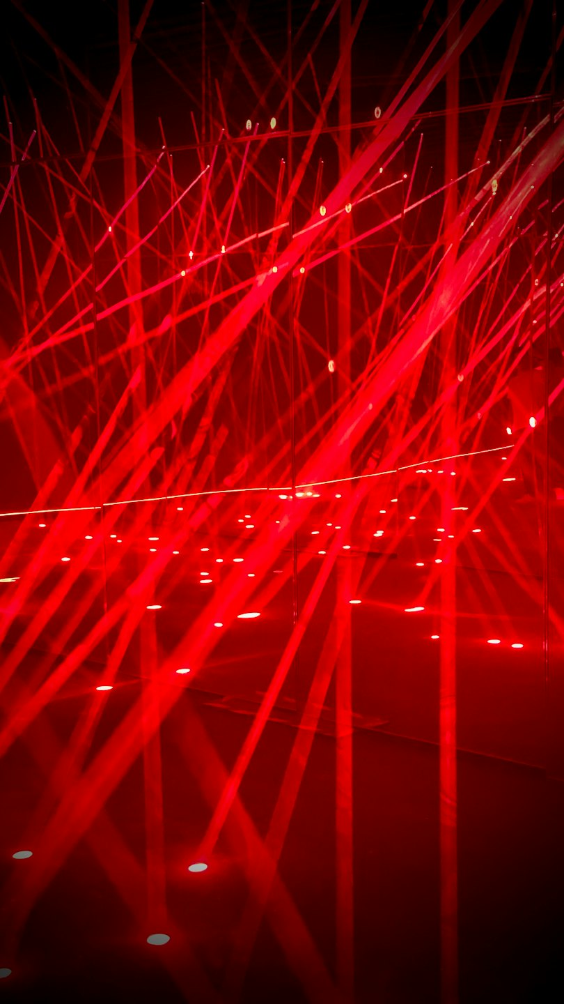 Red laser beams crisscross over a reflective indoor floor.