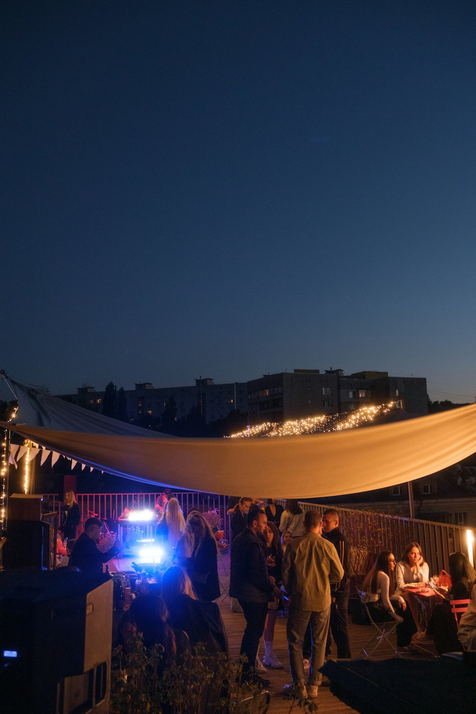 People dancing and socializing on a rooftop at night with city lights.