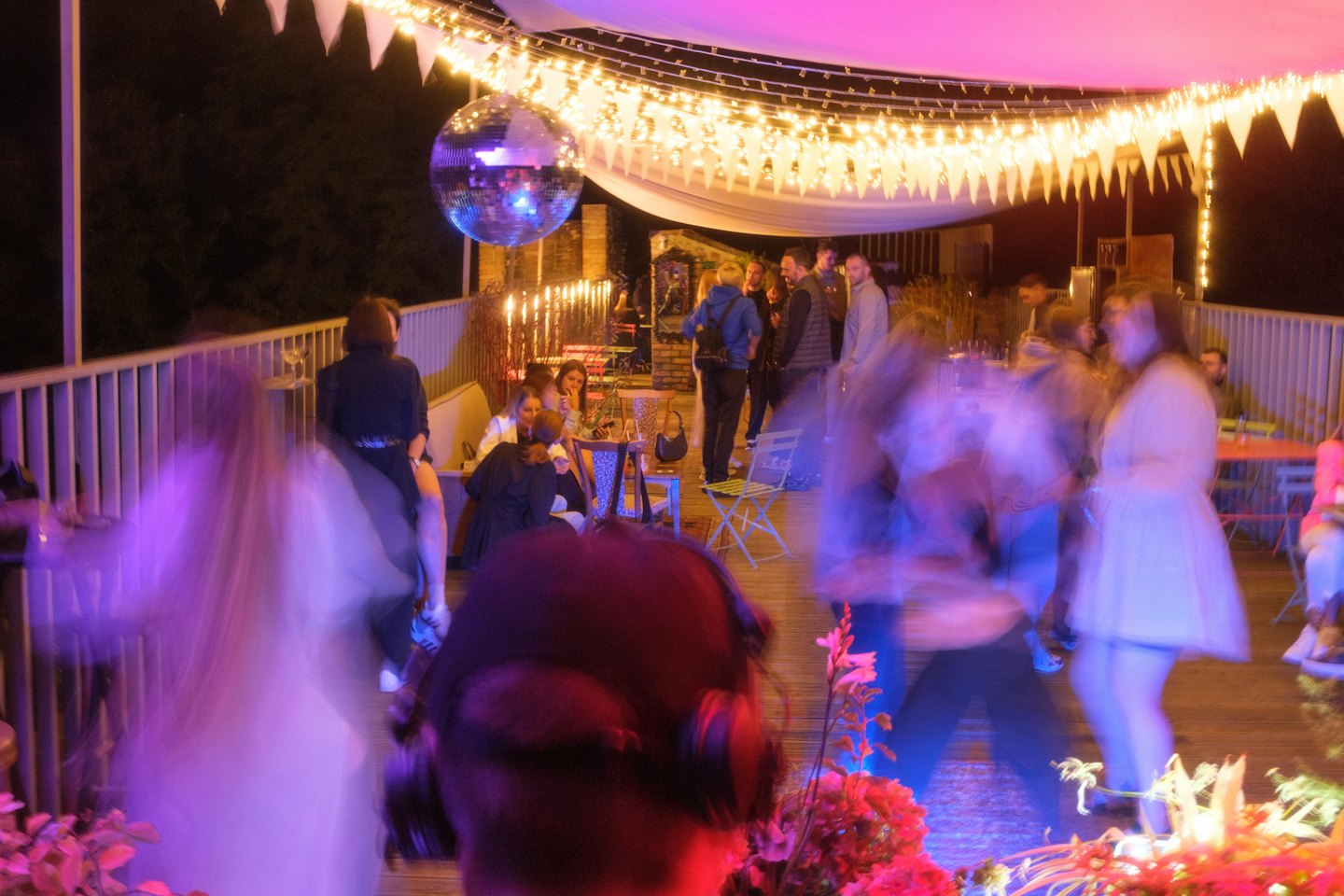 Disco ball and string lights illuminate a lively outdoor party on a terrace.