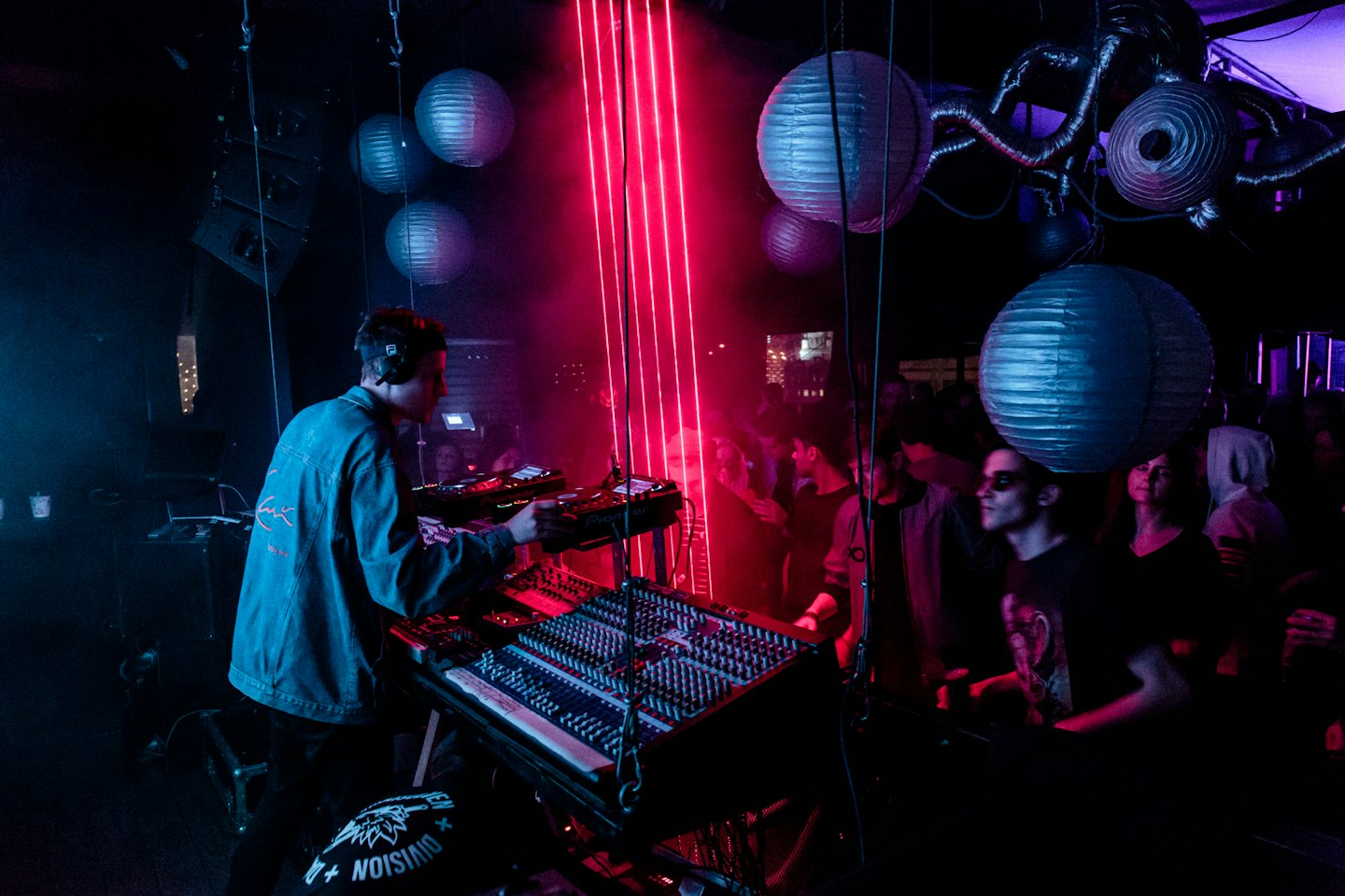 DJ mixing music in a vibrant nightclub with red neon lights.